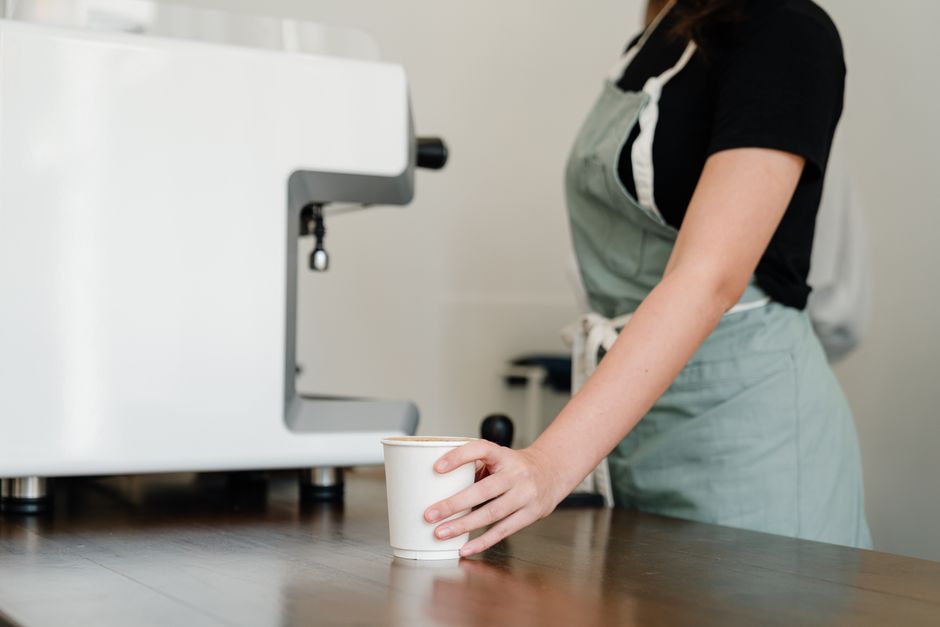 A close-up of a host's hands offering a warm mug of coffee to a guest, representing a simple, sweet gesture of hospitality and care.