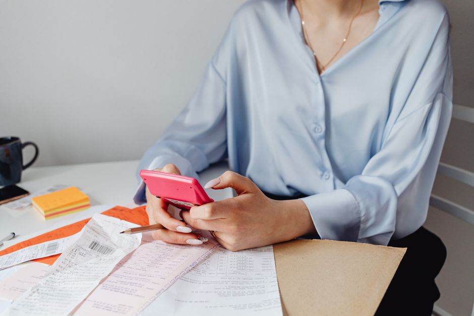 An overhead view of a person using a calculator and writing in a notebook at a clean, modern desk, illustrating financial planning.