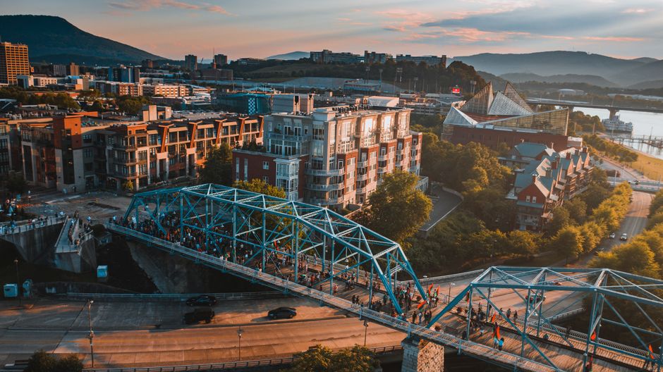 Wide shot of the iconic Walnut Street Bridge in Chattanooga, Tennessee, on a bright, sunny day, with the city skyline and ...